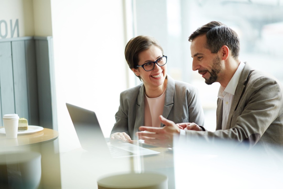 Two professionals, having a conversation while working together on a laptop